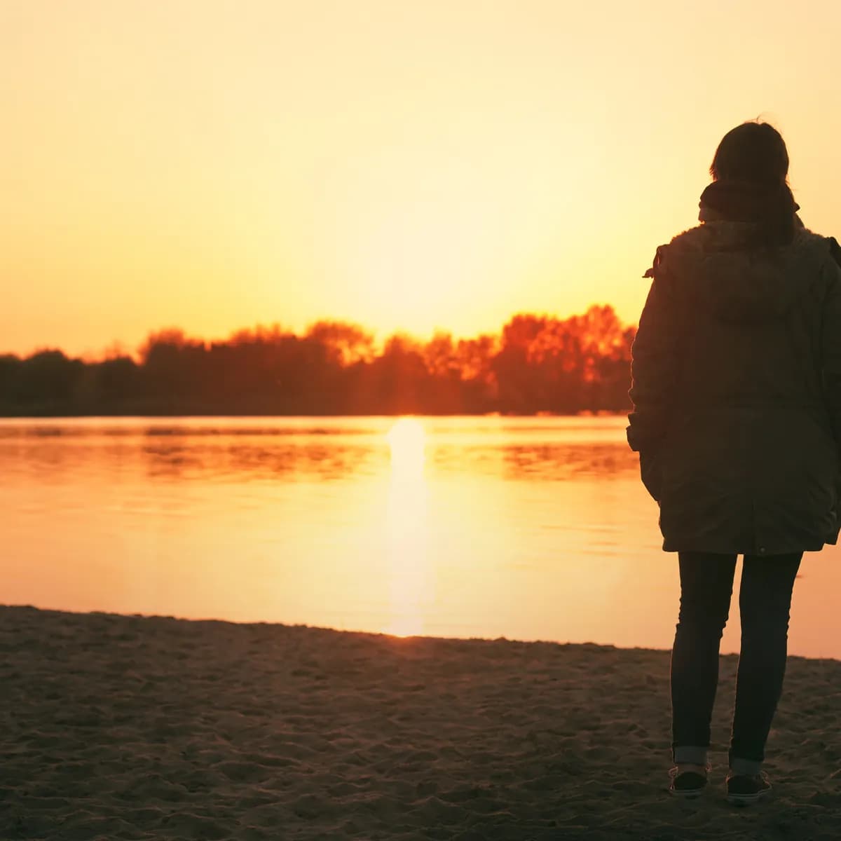 Woman by a lakeshore at sunset, reflecting on her path of growth