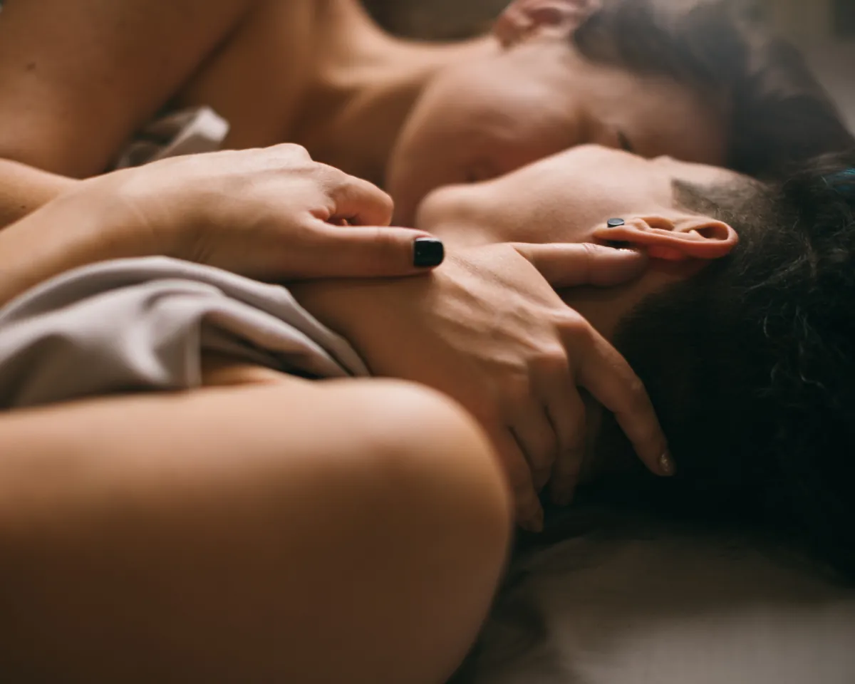Two people lying together in bed in a dim, close embrace
