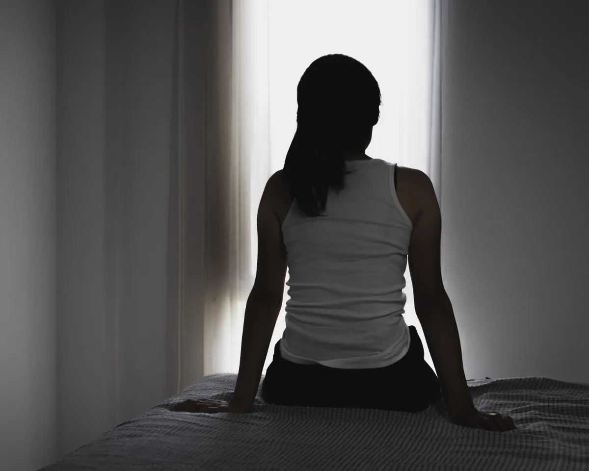Silhouette of a woman sitting on a bed, facing a bright window