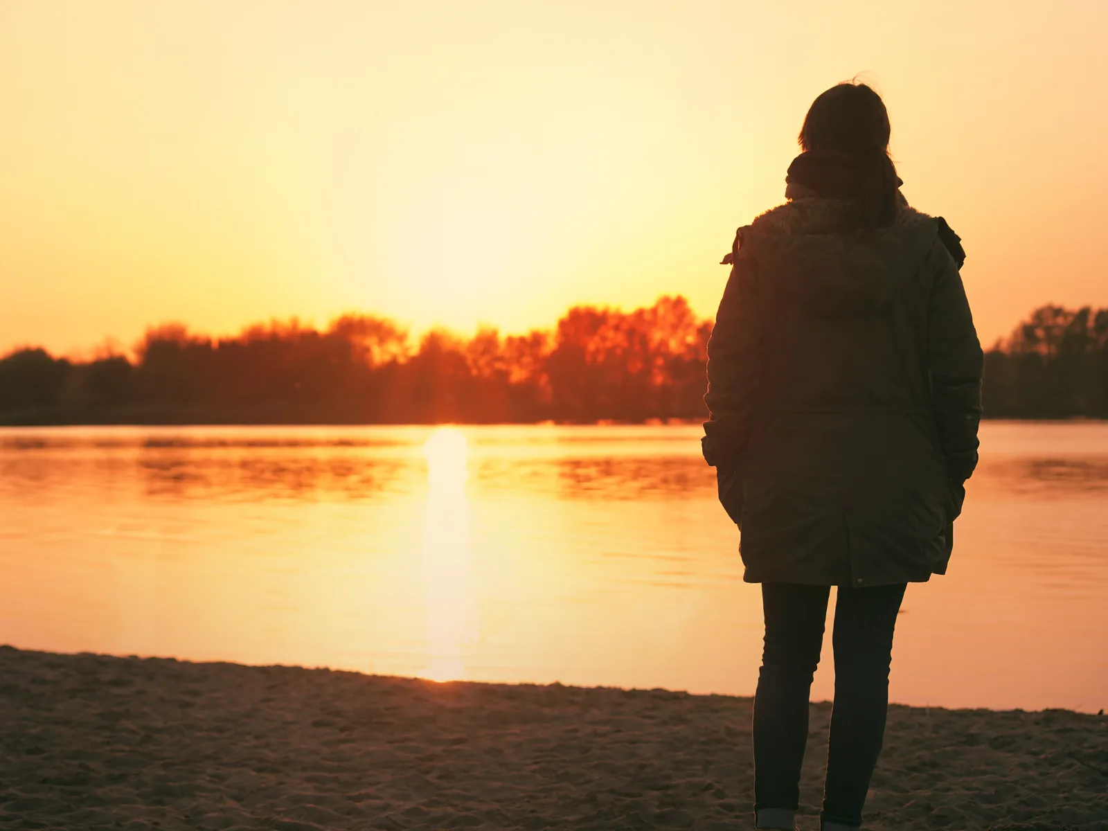 Woman standing at a lakeshore at sunset, reflecting on loss