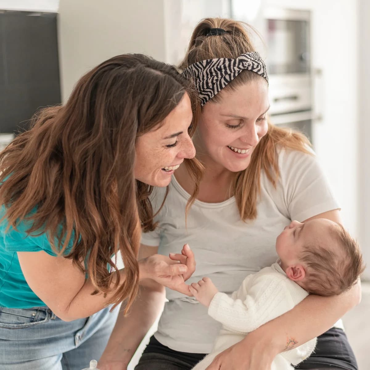 Two mothers smiling at their baby, embracing a new life chapter