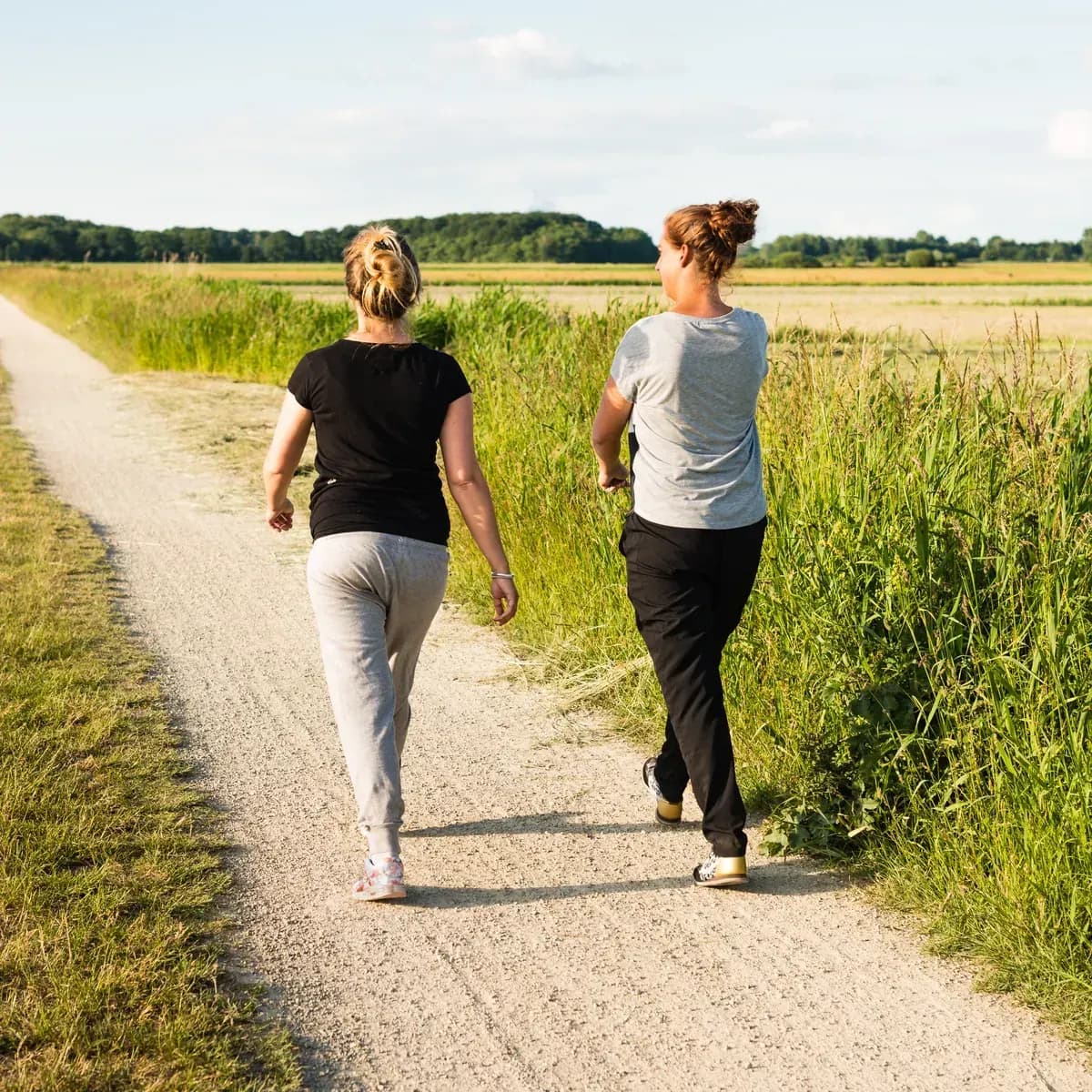 Two women walking together along a sandy path, in connected conversation