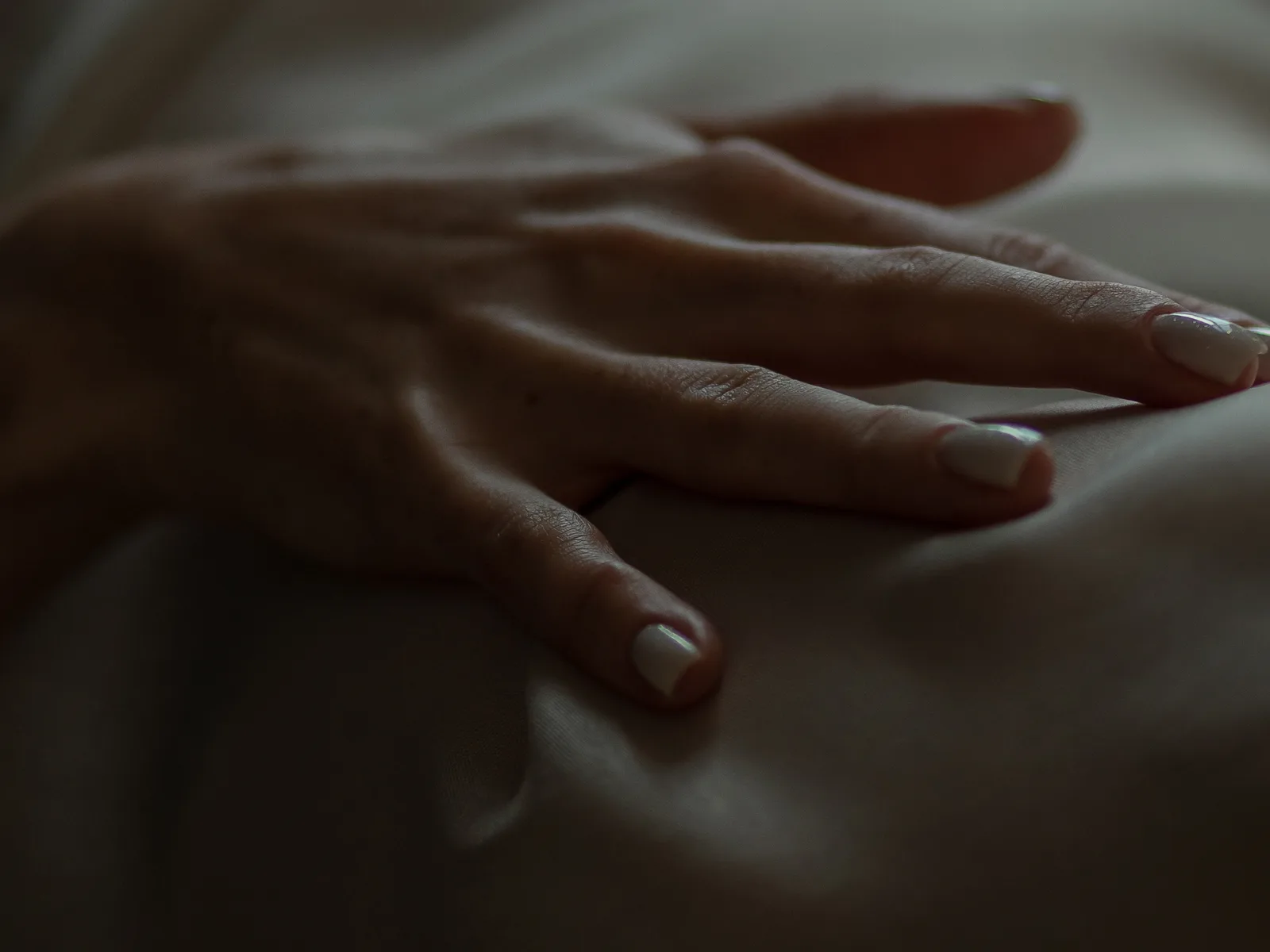 A woman's hand resting on soft bedsheets in low light