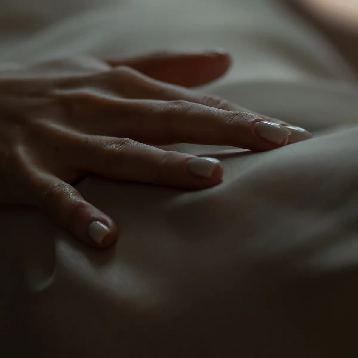 A woman's hand resting on bedsheets in soft, low light