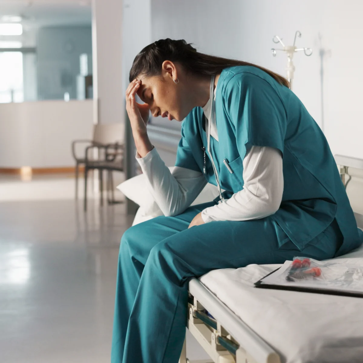 Woman in healthcare scrubs sitting quietly, weighed down by professional stress