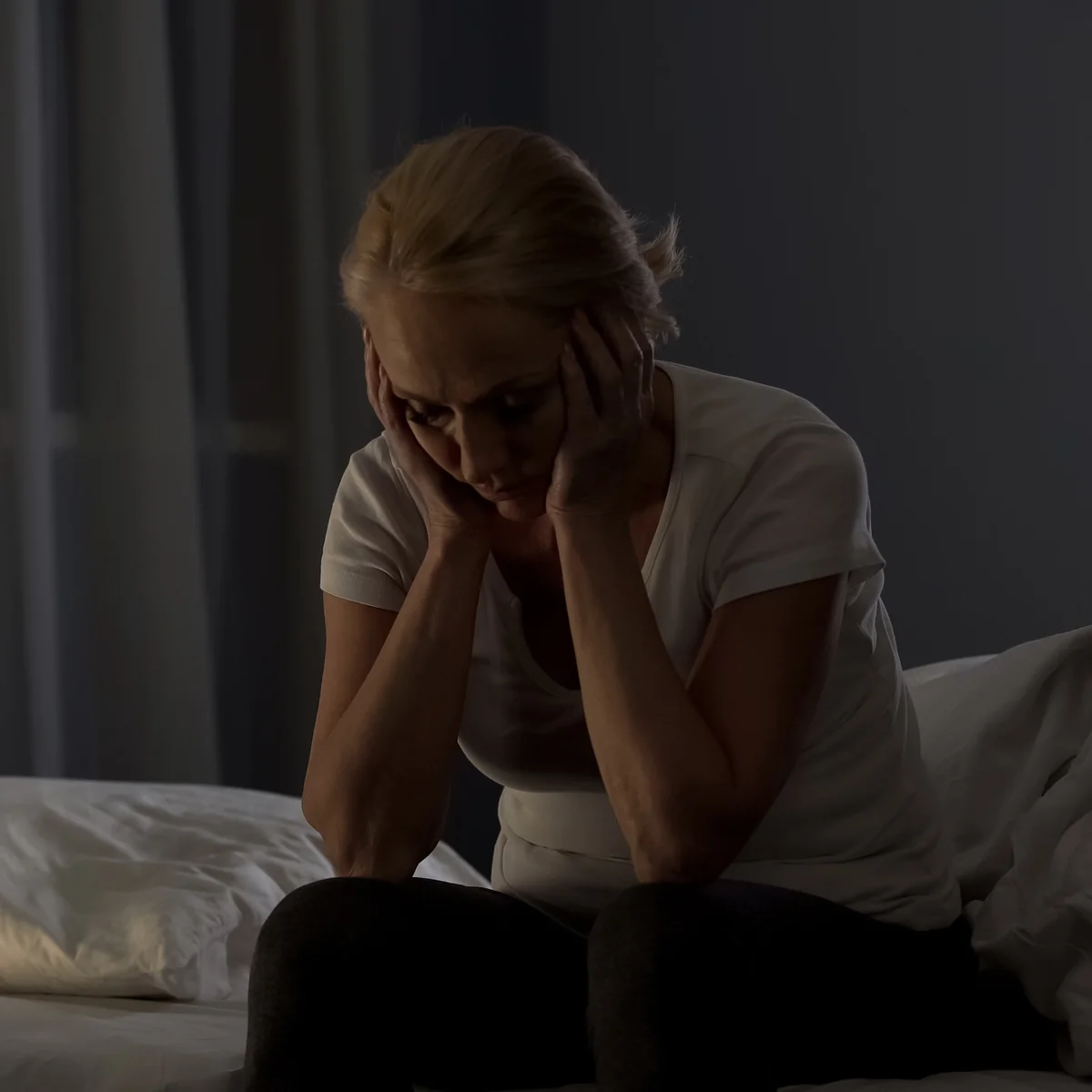Woman sitting on the edge of her bed at night, awake with the weight of trauma